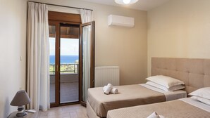 Ett hotellrum med två sängar, havsutsikt, en takfläkt och ett fönster med gardiner.