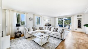 Amplia sala de estar con un sofá seccional en forma de L, una mesa de centro y vistas al exterior a través de grandes ventanales.