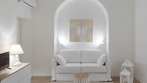 A minimalist white living room with a white sofa, a small round side table, a flat-screen TV, and a white lamp. - Vatican home for seven people  (Rome)