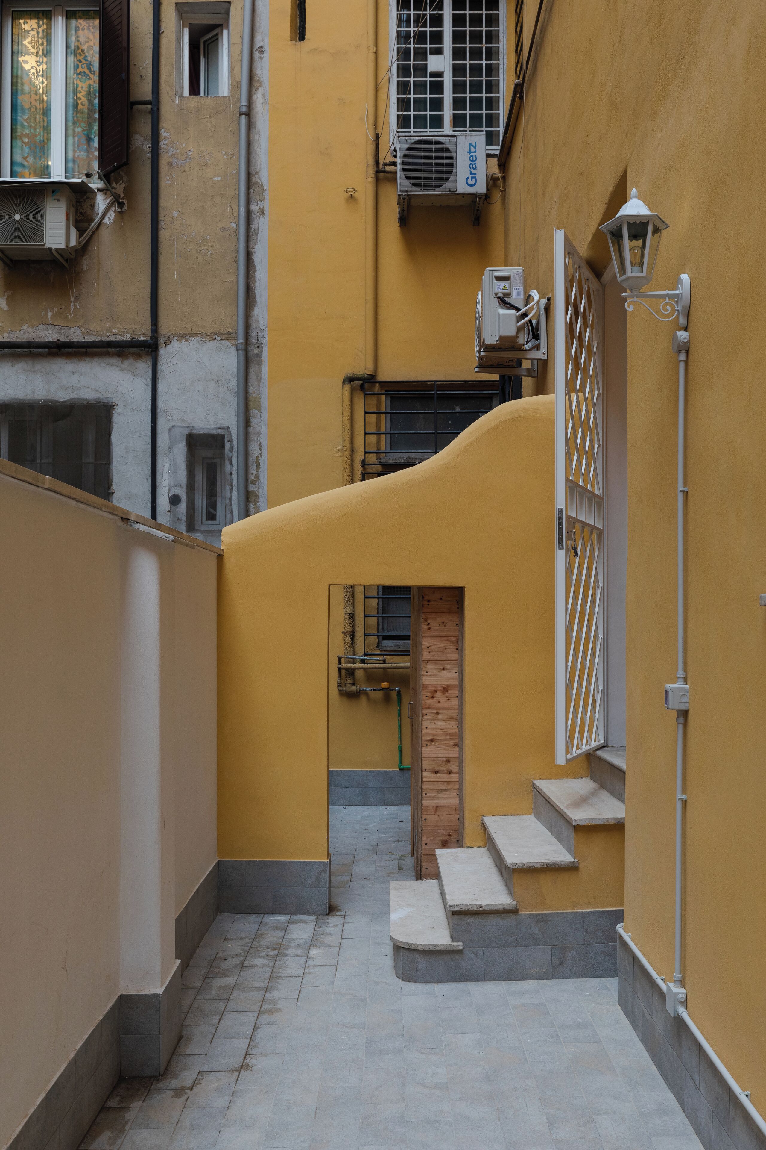 A narrow alleyway with a yellow wall, a wooden door, and a metal gate.