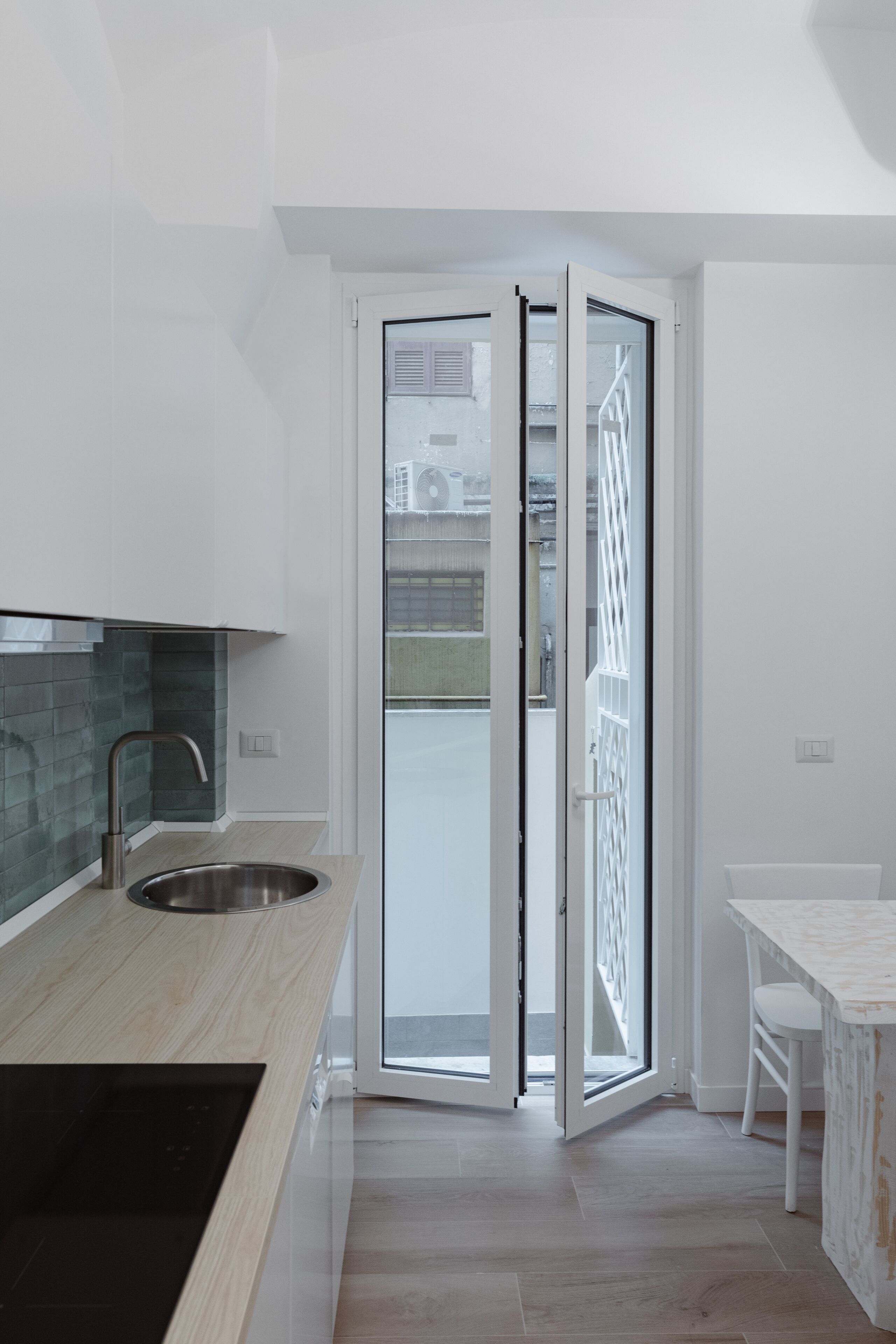 A modern kitchen with a stainless steel sink, a wooden countertop, and a sliding glass door leading to a balcony.