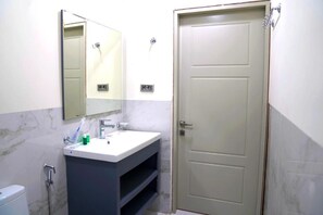 A bathroom with a white sink, a mirror, a door, and a toilet. - zengezurharmonyhotel (Ismailli)