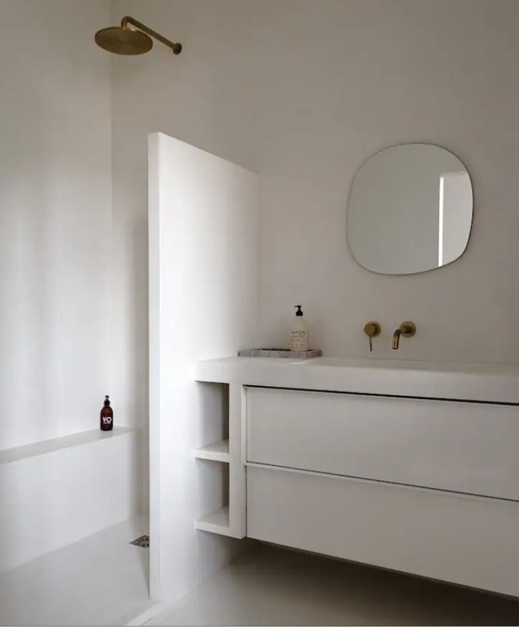 Un bagno minimalista con un mobile lavabo bianco, uno specchio rotondo e una doccia con soffione a mano.