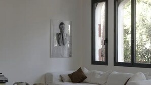 A modern living room with a white sofa, a coffee table, and a bookshelf. There are two windows with black frames, and a painting is visible on the wall. - Beautiful villa in Pyla, 2 min walk from beach (La Teste-de-Buch)
