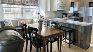A modern kitchen with white cabinets, a microwave, stove, and a coffee maker. There is a dining area with a wooden table and chairs. - Hear SDC - Outdoor Pool- Walk to Lake - King Bed (Branson)