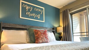 A hotel room with a bed, pillows, a wall sign, a lamp, and a window with curtains. - Hear SDC - Outdoor Pool- Walk to Lake - King Bed (Branson)