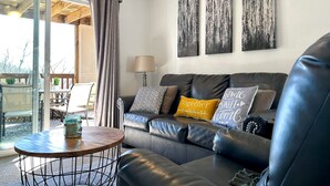 A modern living room with a leather sofa, a round coffee table, and a glass door leading to an outdoor area. - Hear SDC - Outdoor Pool- Walk to Lake - King Bed (Branson)