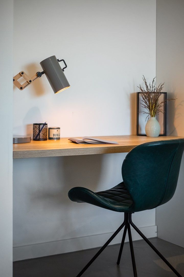 A workspace with a desk, a chair, a desk lamp, a candle, and a vase with dried plants.