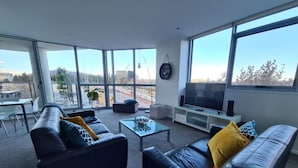 Ein modernes Wohnzimmer mit einem großen Fenster, einer Sofagarnitur, einem Couchtisch und einem Flachbildfernseher.