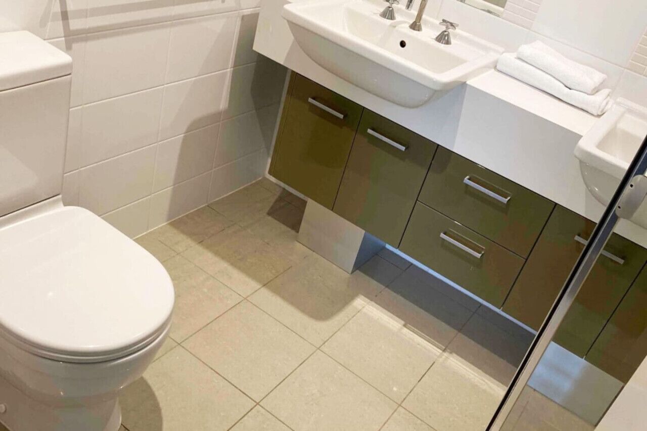 A modern bathroom with a toilet, two sinks, and a mirror.