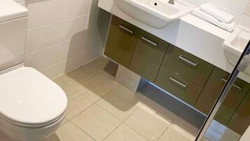 A modern bathroom with a toilet, two sinks, and a mirror.