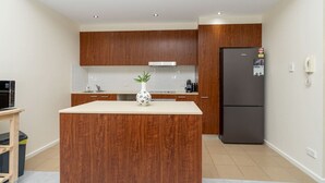 A modern kitchen with wooden cabinets, a central island, a refrigerator, and a small table with a plant. - Absolutely spacious APT unit between ANU and City (Canberra)