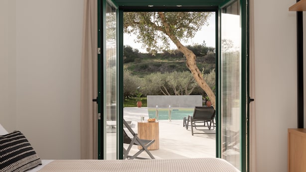 Un dormitorio con cama, una mesita de noche de madera y vistas a un área de piscina exterior con sillas y una mesa.