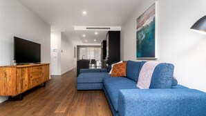 A modern living room with a sectional sofa, wooden entertainment unit, and a large painting. - Contemporary Tri-Level APT in a Prime Central Spot (Braddon)