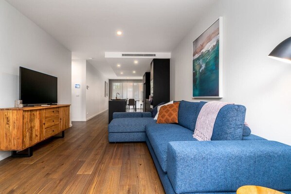 Un salon moderne avec un canapé d’angle, un meuble de rangement en bois et un grand tableau.