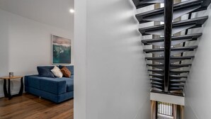 A modern living room with a blue sofa, a painting on the wall, and a unique spiral staircase. - Contemporary Tri-Level APT in a Prime Central Spot (Braddon)