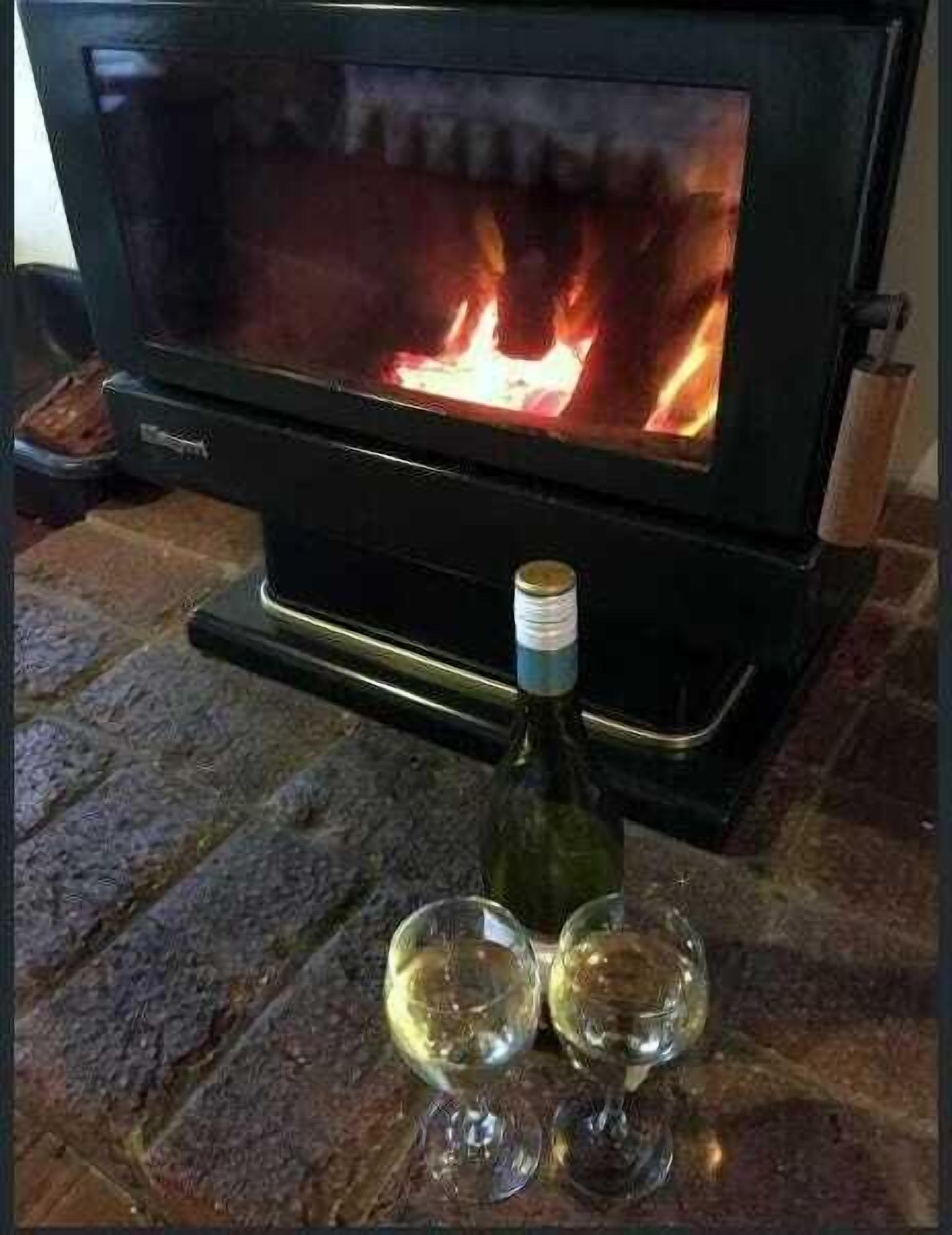 A wood-burning stove with a bottle and two glasses on a stone floor.