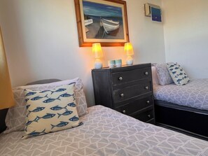 A bedroom with two beds, each with patterned bedding and matching pillows. There is a dresser with drawers and a framed painting above it. - 2 Bed Family Bungalow, Wifi, Parking, Garden, Dogs (Pentraeth)