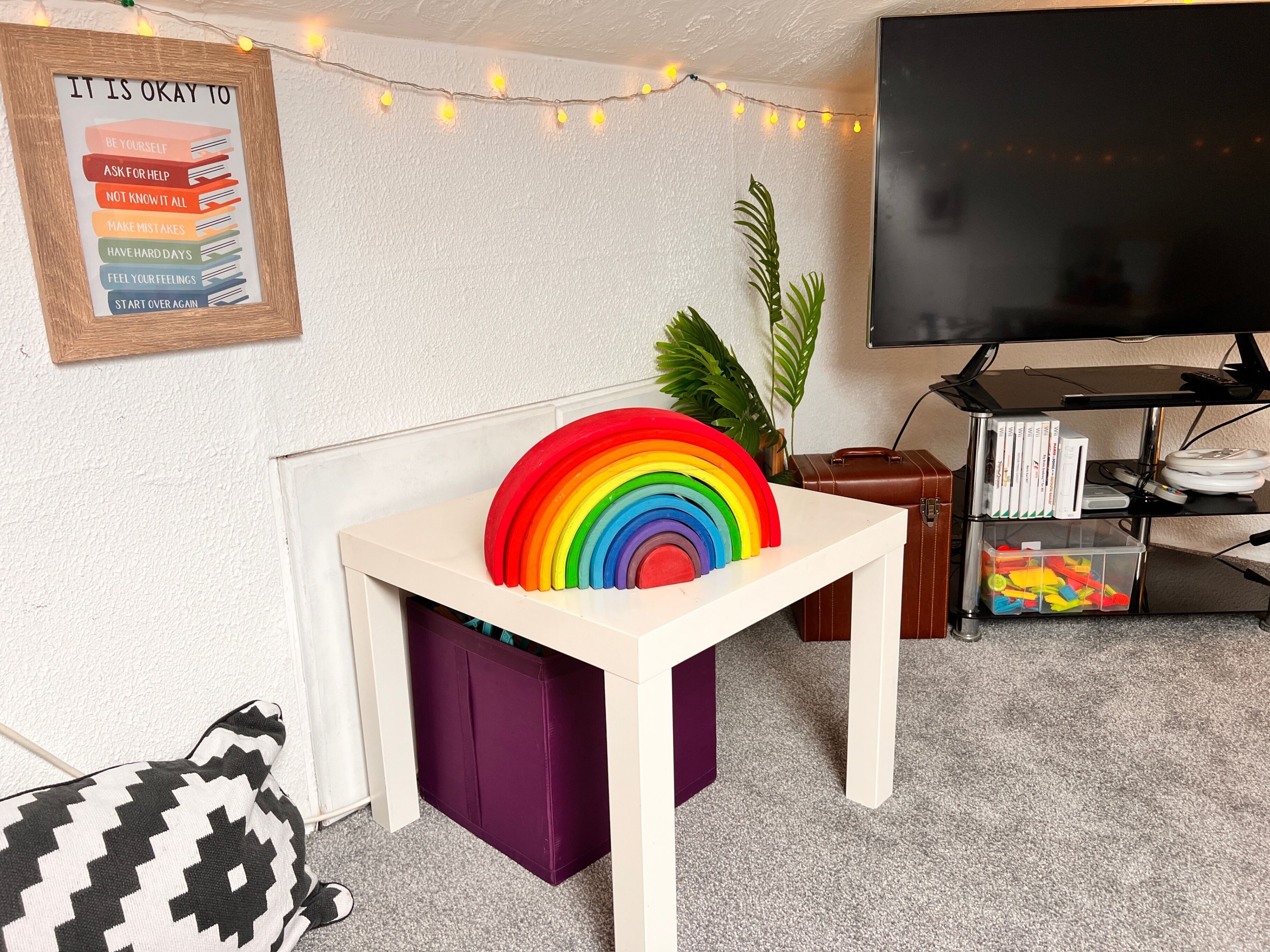 A room with a white table, rainbow-colored object, a framed motivational poster, a television, and a plant.