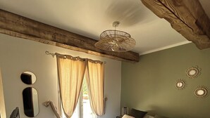 A bedroom with a bed, curtains, a mirror, a television, and a small table. - House at the foot of the Luberon with swimming pool 5 minutes from the village of Lourmarin, (Puyvert)