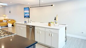 A modern kitchen with white cabinetry, a stainless steel dishwasher, and a black countertop. - Bootlegger’s Nest
 (Anchorage)