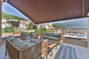 Un balcón con mobiliario exterior, vista a un paisaje urbano y edificios al fondo.