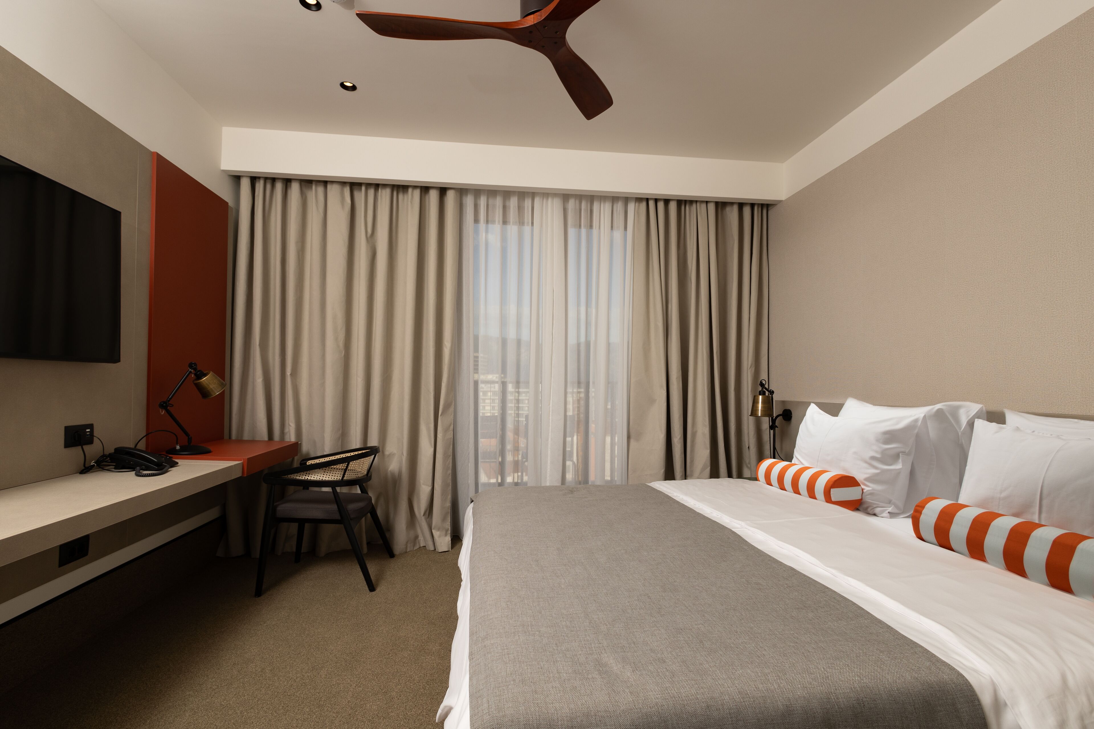 A hotel room with a bed, desk, chair, and a TV mounted on the wall.