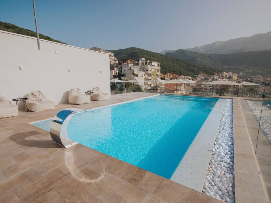 Una piscina con agua cristalina azul, rodeada de baldosas color beige y guijarros blancos.