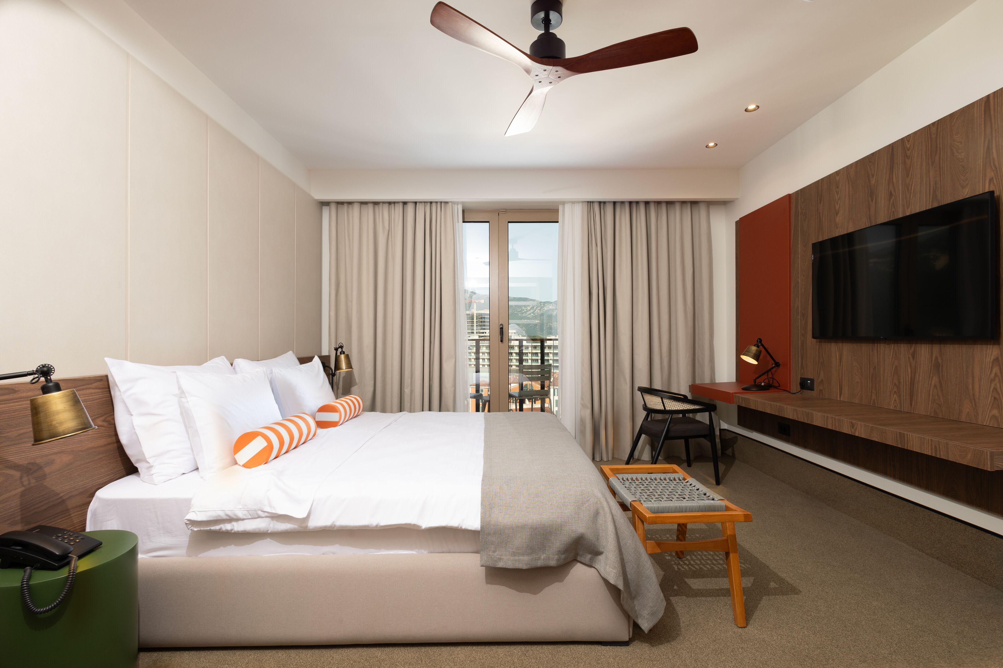Una habitación de hotel moderna con una cama grande, un escritorio, un televisor y un balcón con vista a la ciudad.