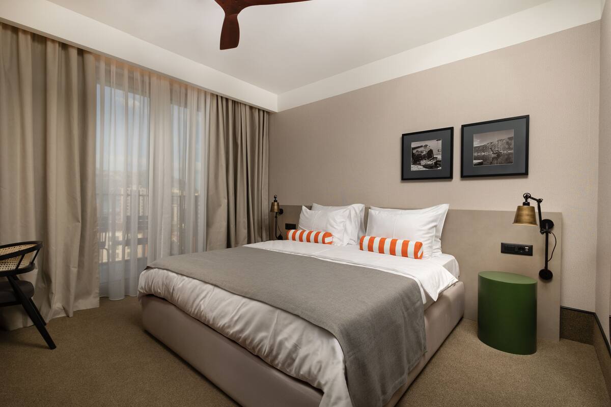 A hotel room with a large bed, a chair, a green side table, and two framed pictures on the wall.
