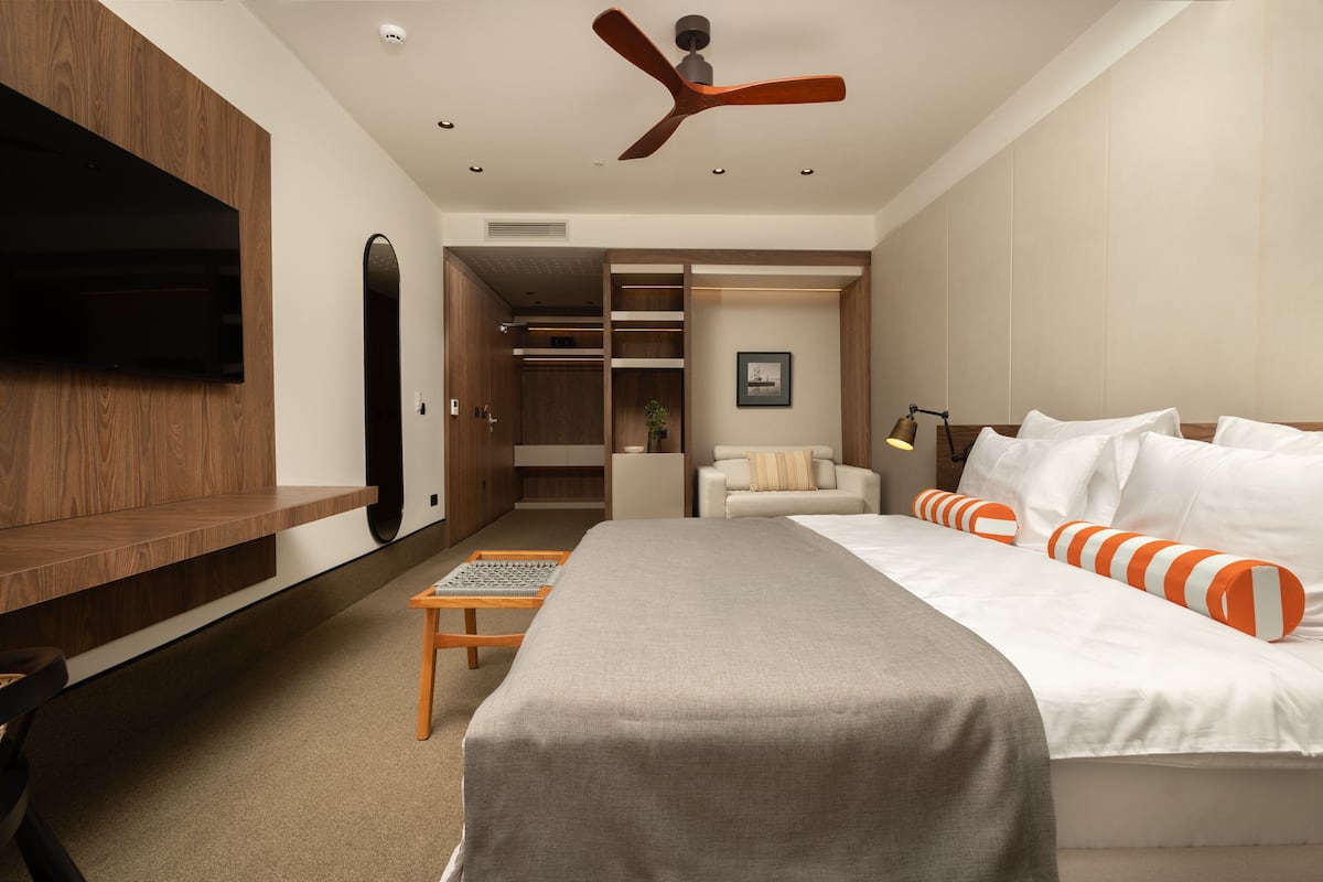 A modern hotel room with a bed, a TV, a ceiling fan, and a walk-in closet.