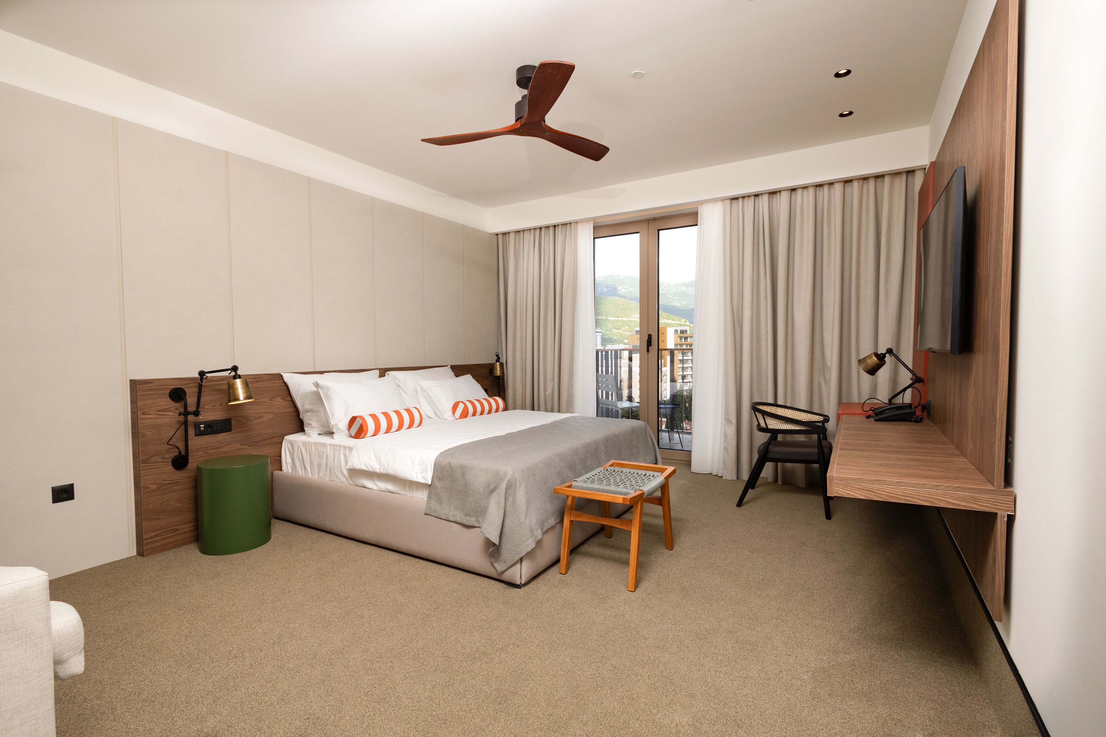 Une chambre d’hôtel moderne équipée d’un lit, d’un bureau, d’une chaise, d’un ventilateur de plafond et offrant une vue sur l’extérieur.