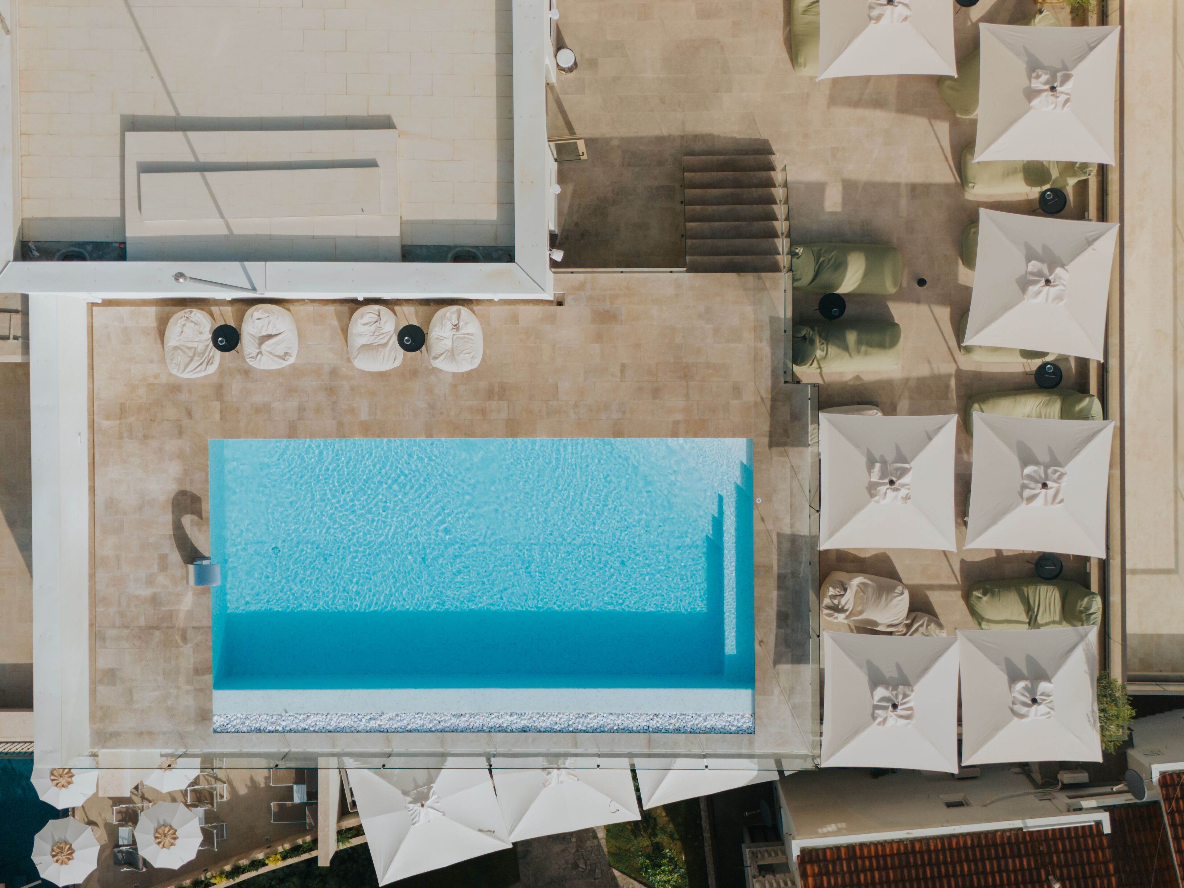 En vy från ovan av ett hotell med en swimmingpool som omges av solstolar och parasoller.