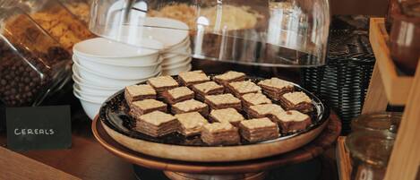 A buffet table with a variety of food items including a bowl of brownies and a glass container labeled "CEREALS".