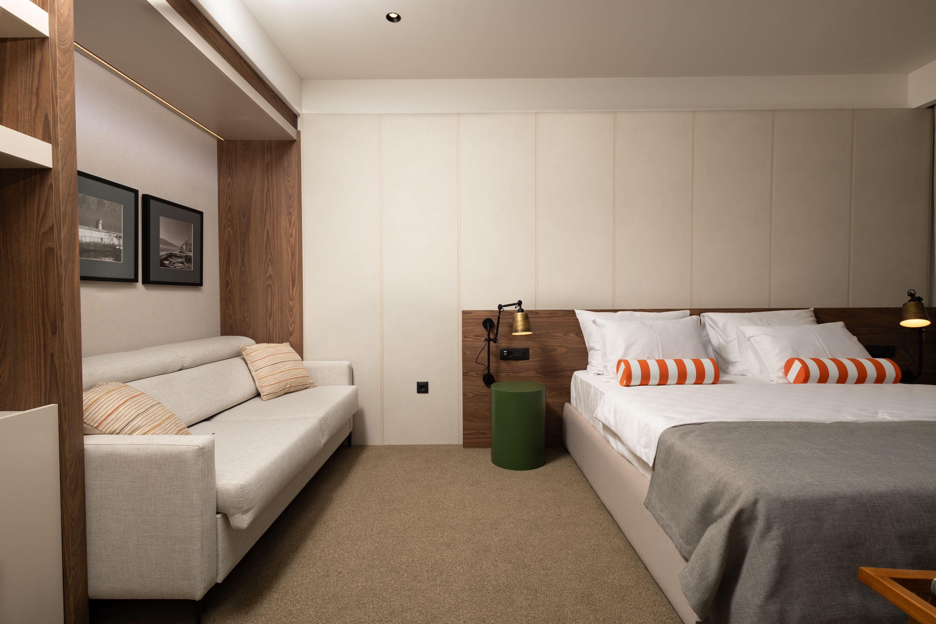 Una habitación de hotel con una cama, un sofá, un cesto de basura verde y cuadros en la pared.
