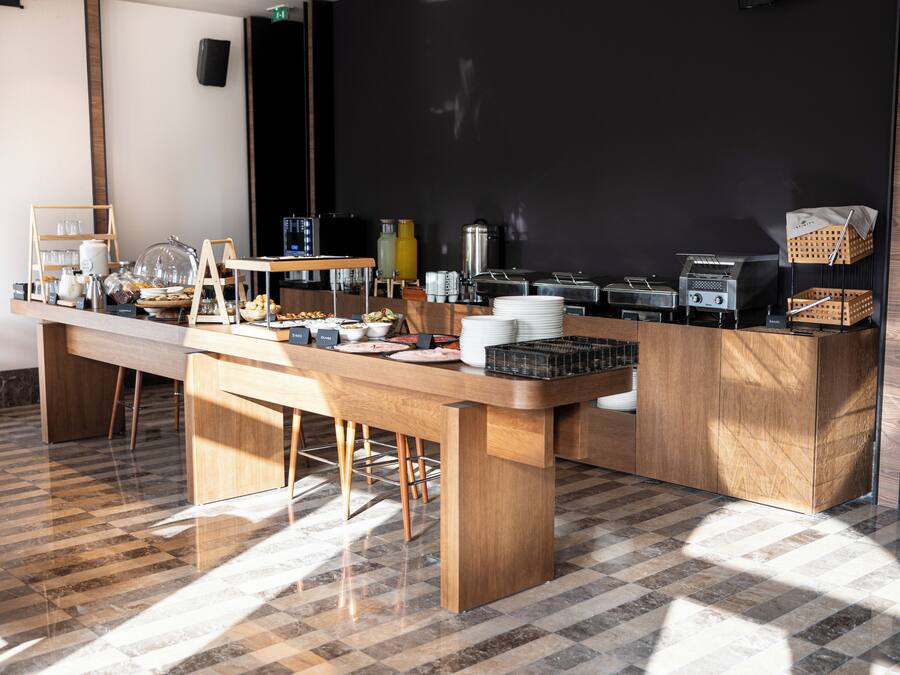 Montaje de un bufé de desayuno con diferentes alimentos, bebidas y utensilios sobre una mesa y mostrador de madera.