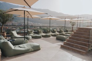 A rooftop terrace with outdoor seating, large umbrellas, and a view of a cityscape and mountains. - Infinity Hotel & More (Budva)