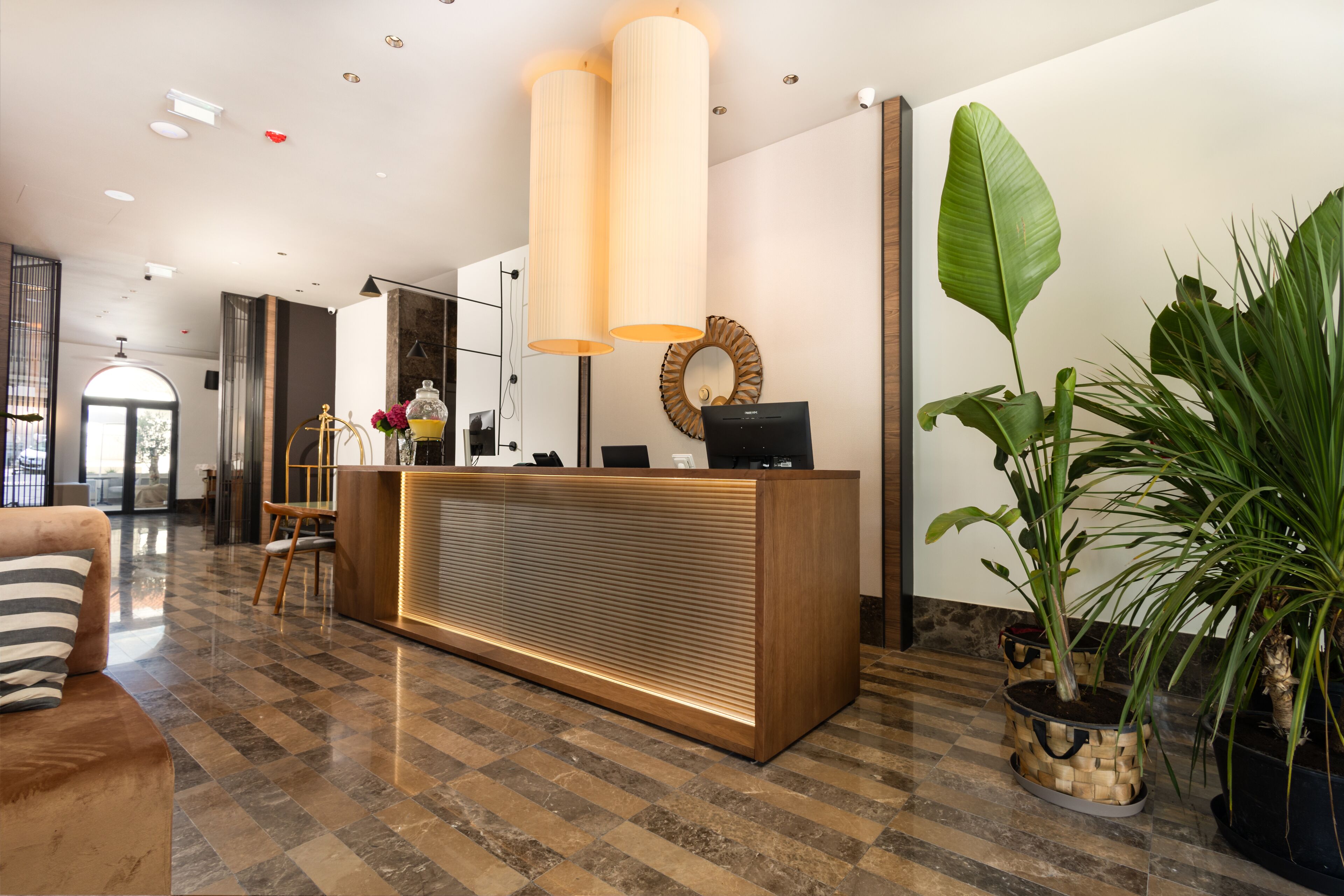 A reception area with a wooden reception desk, two large pendant lights, a mirror, and a large potted plant.