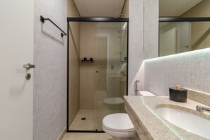 A modern bathroom with a glass-enclosed shower, a white toilet, and a granite countertop with a sink. - Studio next to Congonhas (São Paulo)