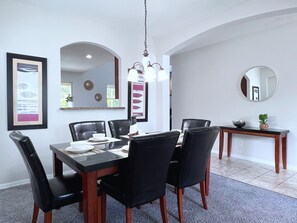 A dining area with a rectangular table, six black chairs, a hanging light fixture, a mirror, and framed artwork on the walls.