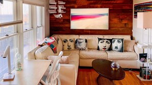 Una sala de estar moderna con techo de madera, un cuadro abstracto grande, un sofá con cojines estampados y una mesa de centro.