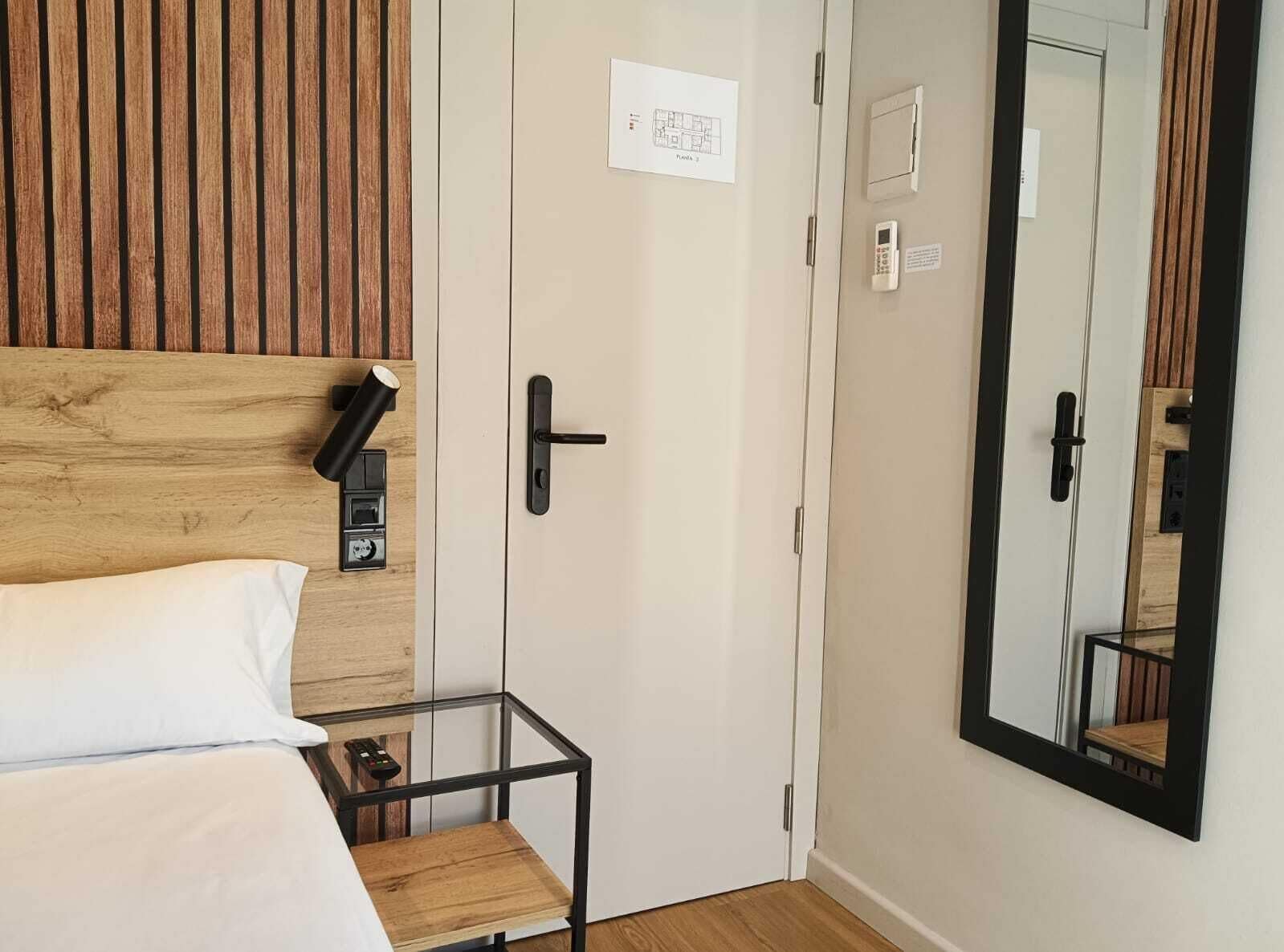Une chambre d’hôtel avec une tête de lit en bois, un lit avec une literie blanche, une table en verre et un grand miroir.
