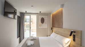 Una habitación de hotel moderna con una cama grande, un televisor de pantalla plana montado en la pared, un cabecero de madera y vistas al balcón exterior.