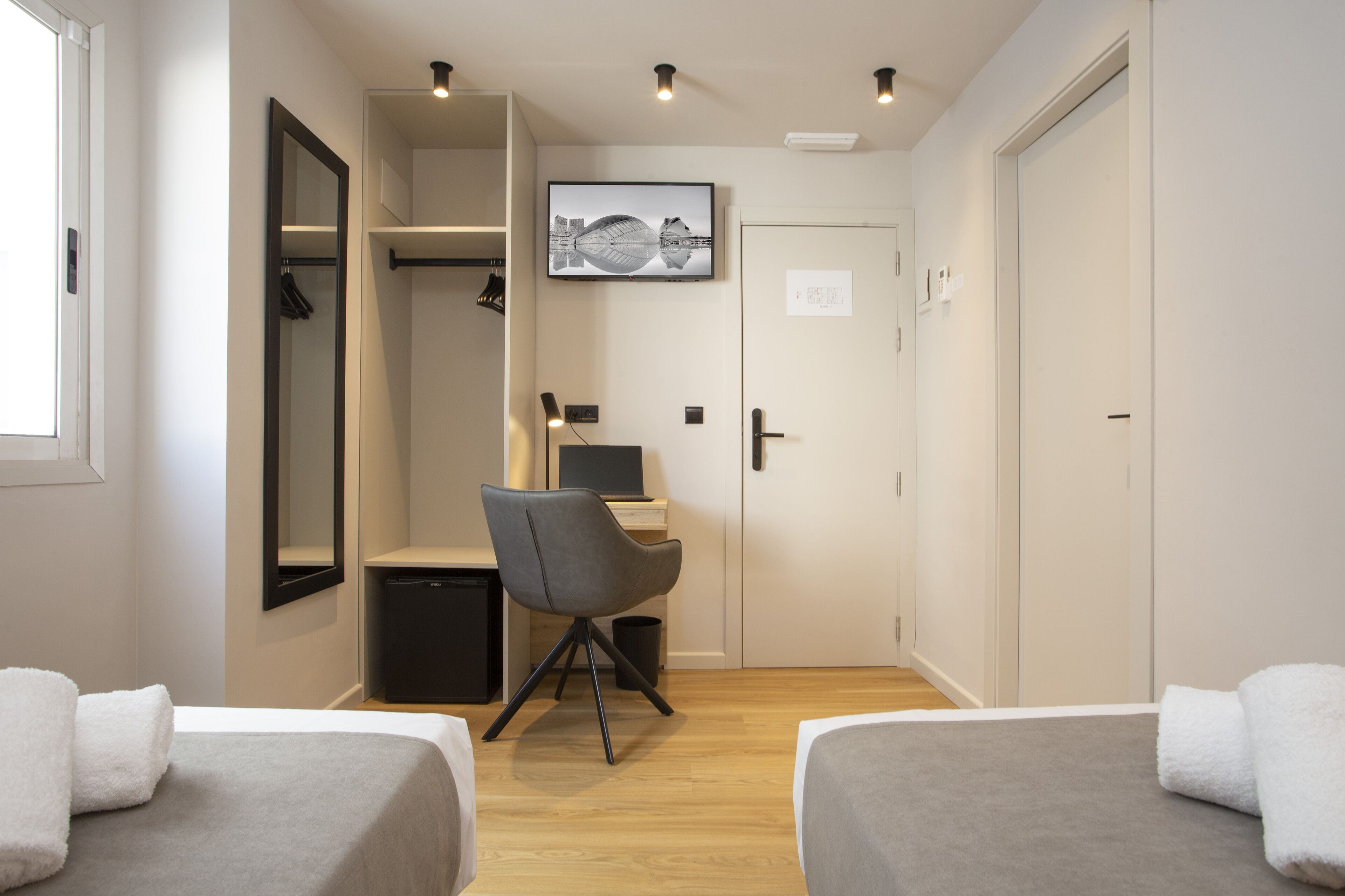 A hotel room with two beds, a desk, a chair, a mirror, a TV, and a wardrobe.