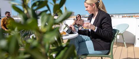 A rooftop terrace with a dining table, chairs, and a person using a tablet.