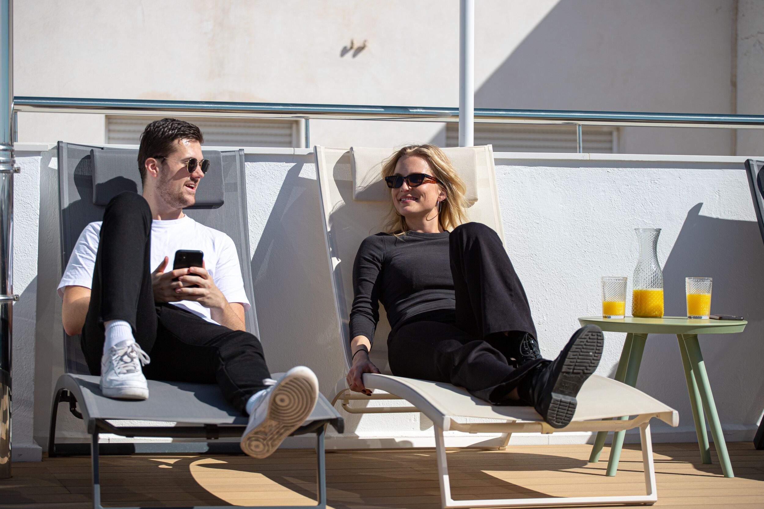 Two people relaxing on sun loungers with a table and drinks nearby.