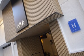 L’entrée d’un hôtel, avec une enseigne indiquant « VILA HOTEL » et un panneau bleu signalant la présence d’un hôtel.