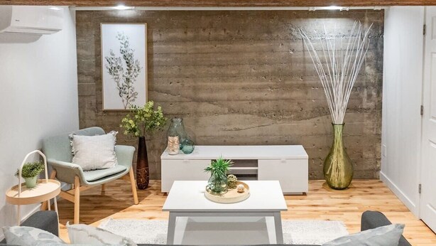 Un salon moderne avec un canapé gris, une table basse blanche, un fauteuil gris et une console blanche. On y trouve un grand vase contenant de longues branches blanches et, au mur, une estampe botanique encadrée.