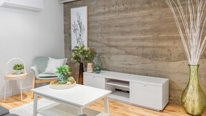 Un salon moderne avec un canapé blanc, une table basse blanche et un meuble de rangement pour appareils électroniques, le tout placé devant un mur à texture.