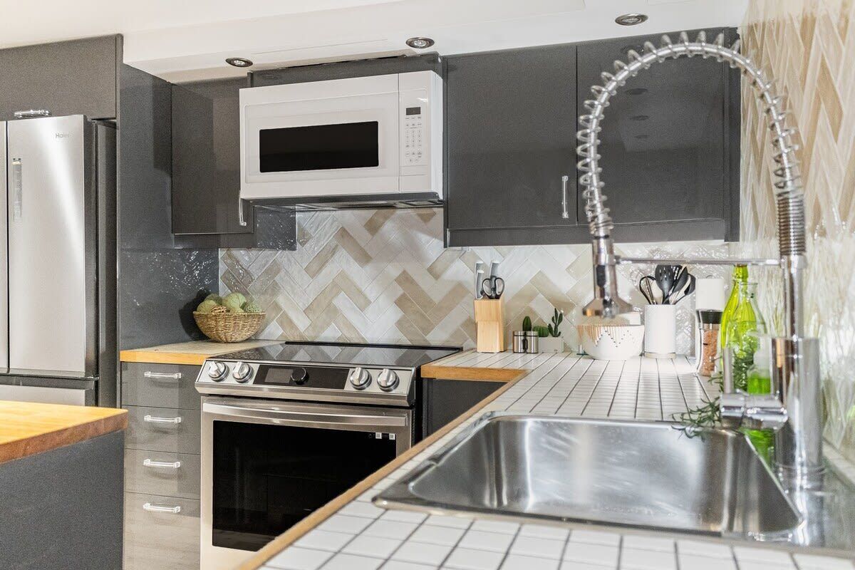 Une cuisine moderne dotée d’appareils électroménagers en acier inoxydable, d’un dosseret de carrelage disposé en motif chevron et d’un évier encastré.